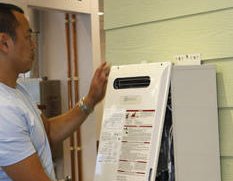 A person standing beside a wall-mounted tankless water heater.