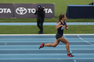 Let ’Em Play – Michelle Cross Track Race Michelle Cross running on a blue track in a track and field race.