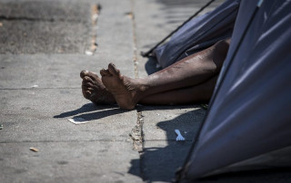 A person’s bare feet extend from a tent on a Los Angeles sidewalk.